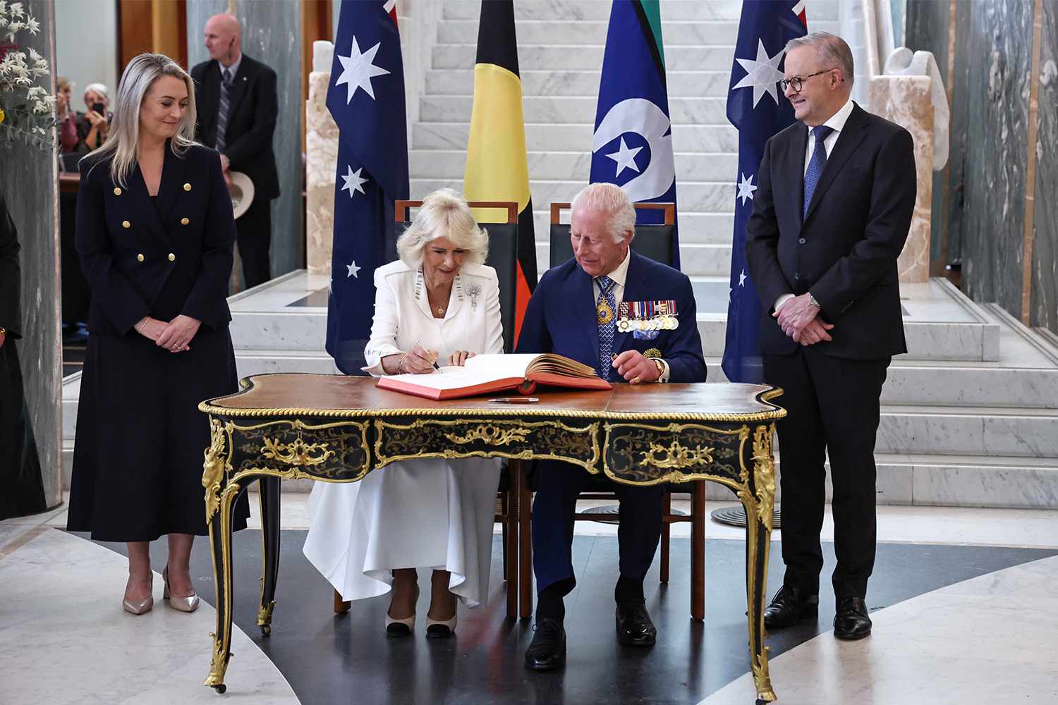 King Charles III and Queen Camilla sign a visitors' book as Prime Minister of Australia Anthony Albanese (R) and his partner Jodie Haydon (L) look on in the Marble Foyer of Parliament House in Canberra on October 21, 2024 in Canberra, Australia