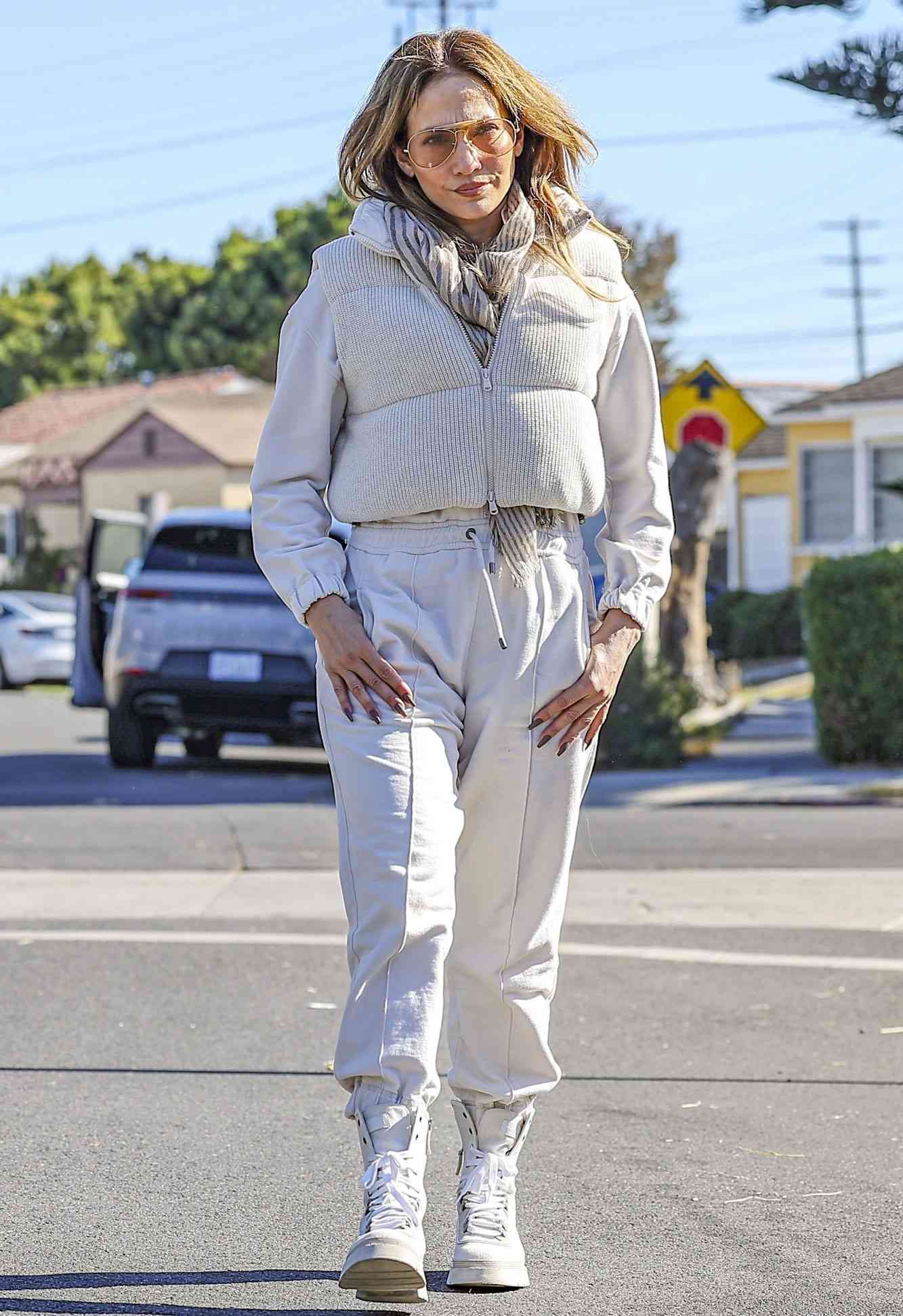 Jennifer Lopez showcased her chic winter style while visiting a friend in Los Angeles. She donned an off-white puffer vest over a white long-sleeve top, paired with jogger-style pants and a beige plaid scarf for a cozy monochromatic ensemble.