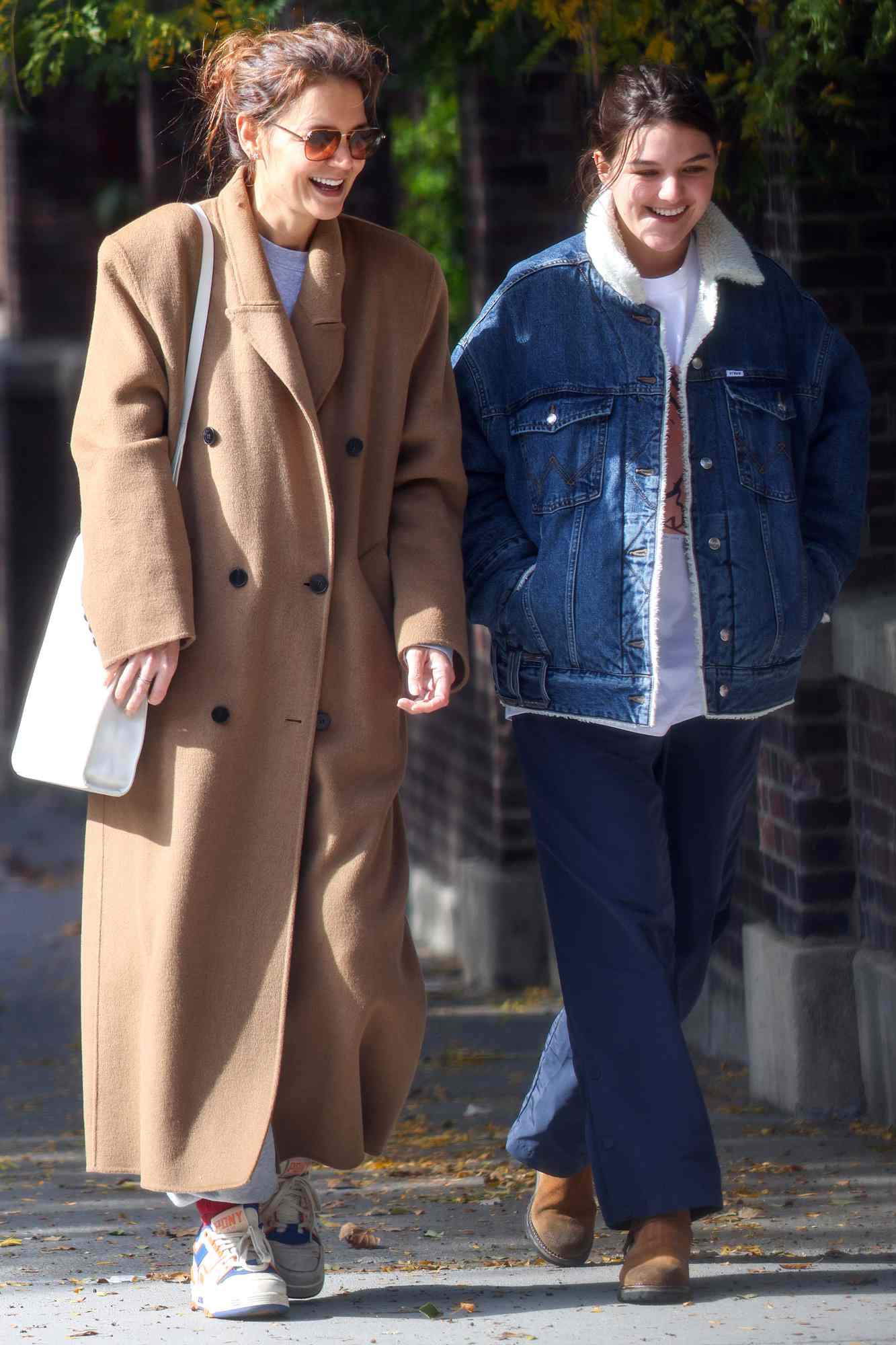 Kate Holmes and Suri Cruise are spotted on a stroll in New York City. The lookalike duo were seen enjoying time together after Suri recently left for college. The 18 year old wore a shearling lined denim jacket, dark, trousers and brown boots. Katie wore a black brown coat, sweater, grey joggers, and vintage sneakers.