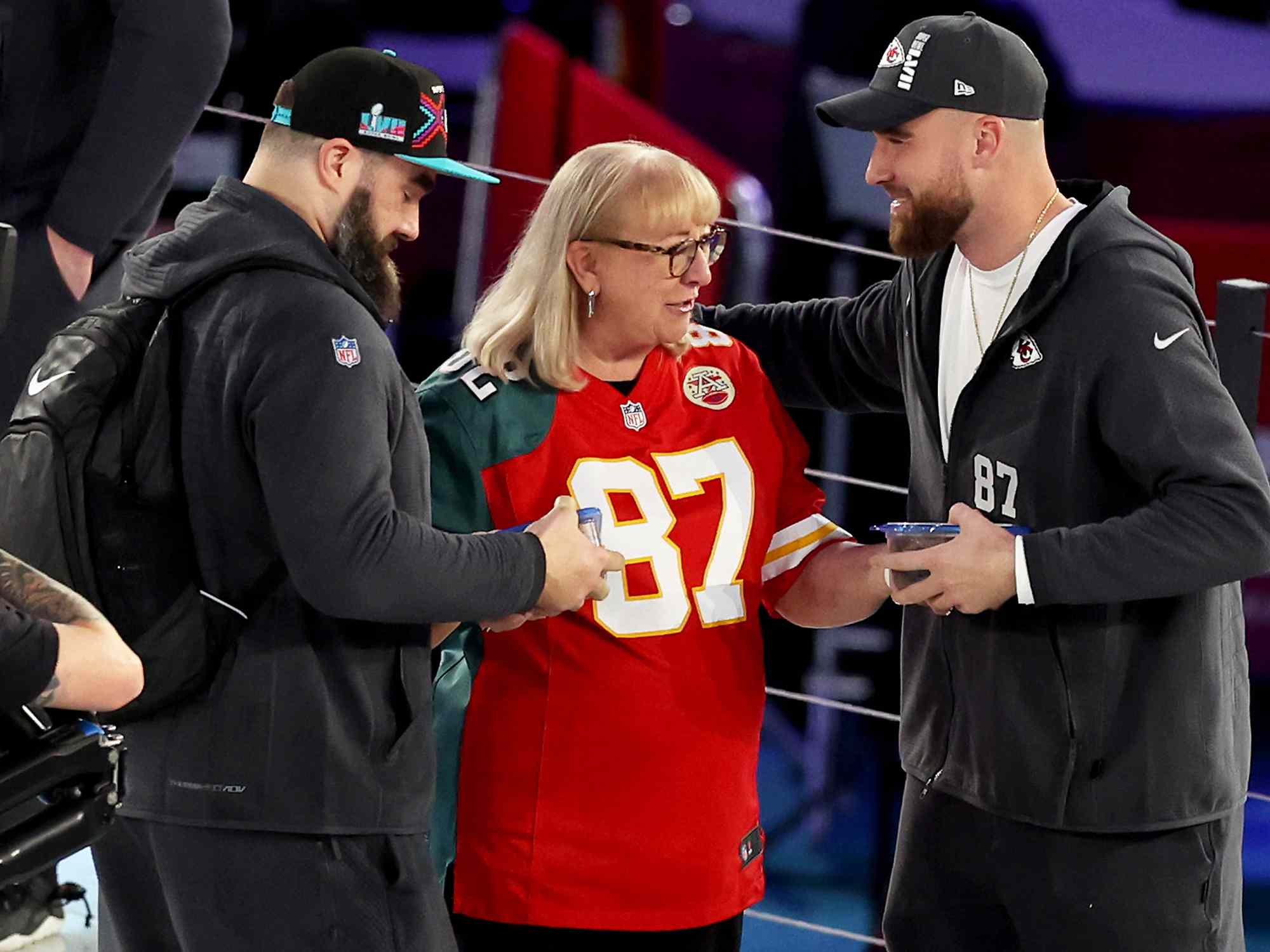 Donna Kelce (C) gives cookies to her son's Jason Kelce (L) #62 of the Philadelphia Eagles and Travis Kelce (R) #87 of the Kansas City Chiefs during Super Bowl LVII Opening Night presented by Fast Twitch at Footprint Center on February 06, 2023 in Phoenix, Arizona